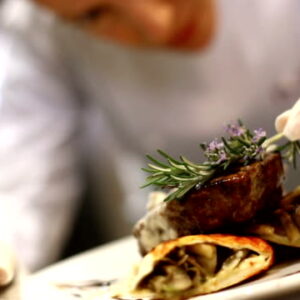 Professional female chef placing finishing touches by putting rosemary on steak just before serving. She's wearing protective gloves when touching ready to eat food.HD 1080